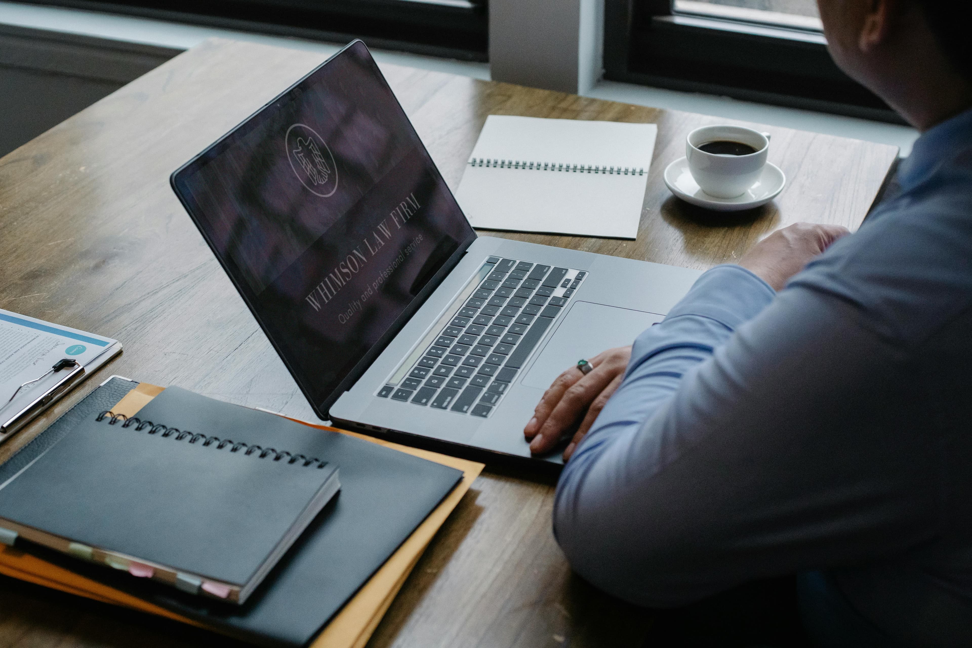 A person working at a desk with a laptop displaying the "Whimson Law Firm" logo, with notepads and a cup of coffee nearby, utilizing various lead generation tools.