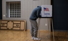 A voter leans over their ballot in a voting booth.