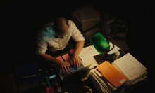 A man looks over a stack of papers in a dimly-lit attorney's office.